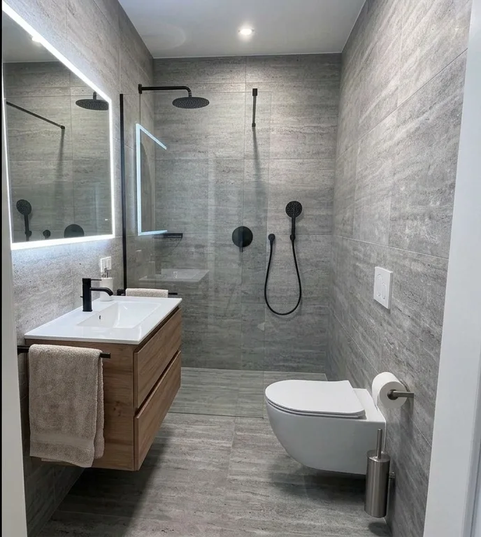 Baño en tonos grises con ducha de obra a ras de suelo y grifería negra mate